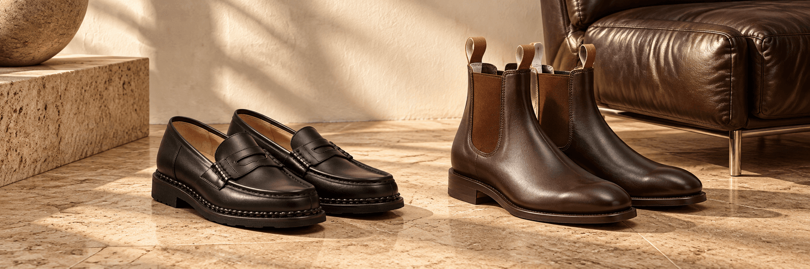 Schwarze Lederloafer und kastanienbraune Chelsea-Boots in einem warmen Ambiente mit Leder und Naturstein